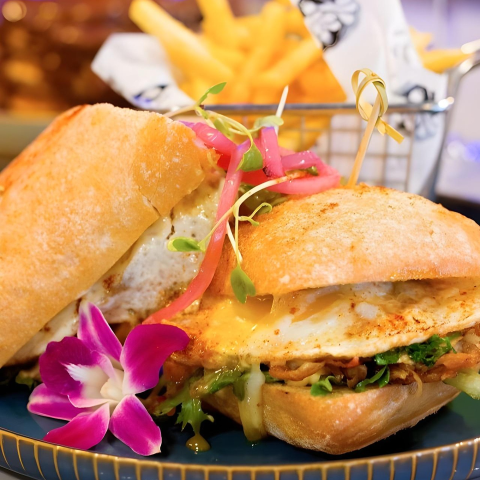 Cuban sandwich with fried egg, pickled onions, and microgreens, served with fries and an orchid.