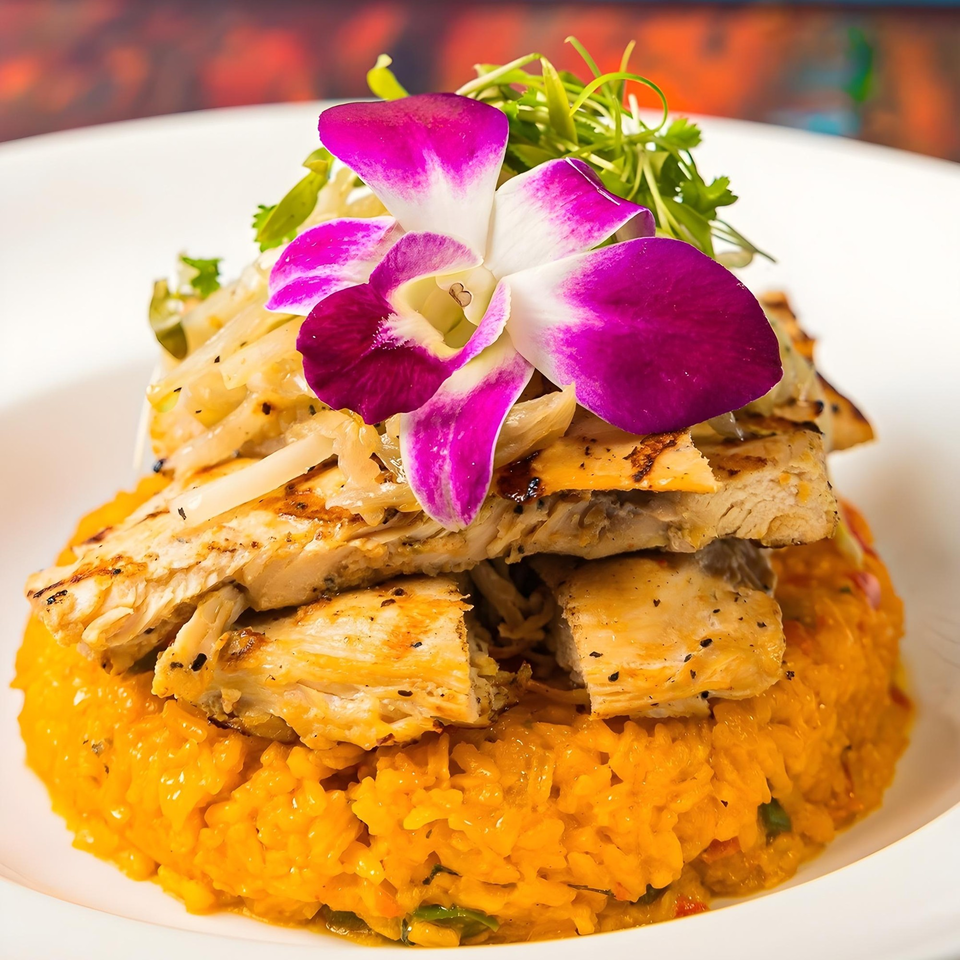 Grilled chicken slices over yellow rice, garnished with pickled onions, cilantro, and a purple orchid.