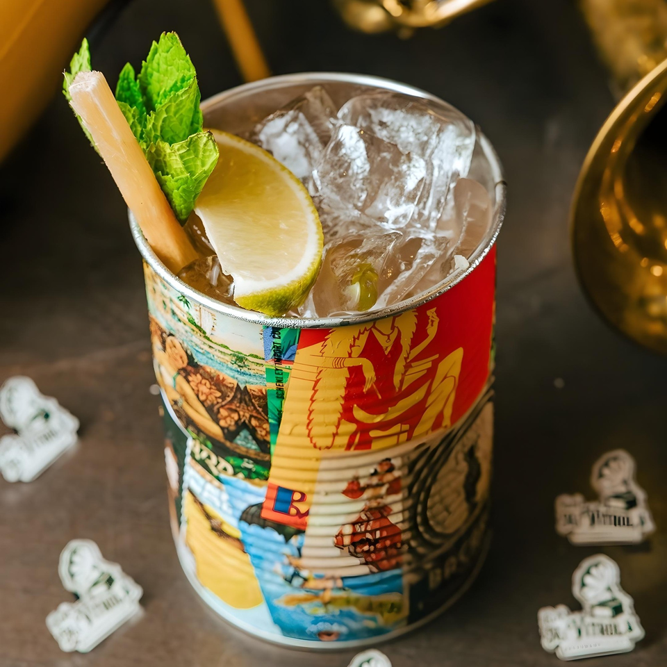 A Cuban cocktail in a colorful can, garnished with sugarcane, mint, and a lime slice.