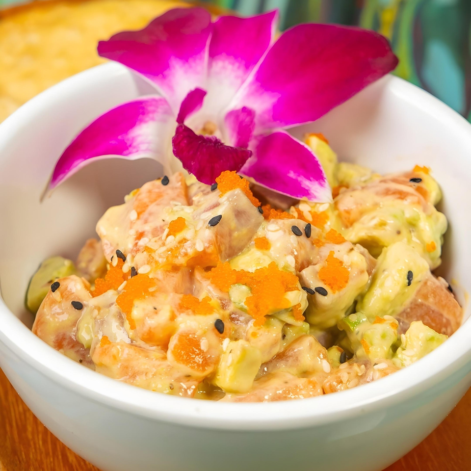 A white bowl of Cafe Mi Vitrola's poke, garnished with a vibrant purple orchid.