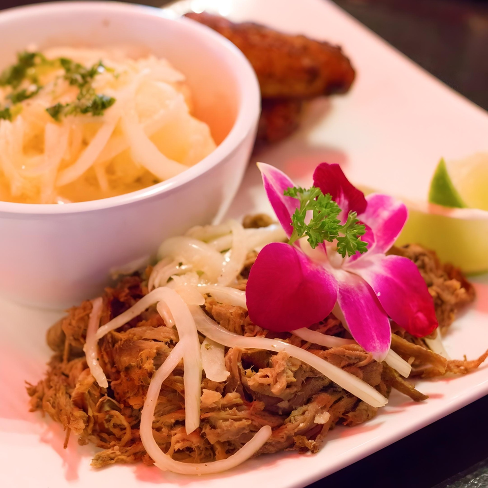 Cuban shredded pork with onions, a side of rice, plantains, and a pink orchid garnish.